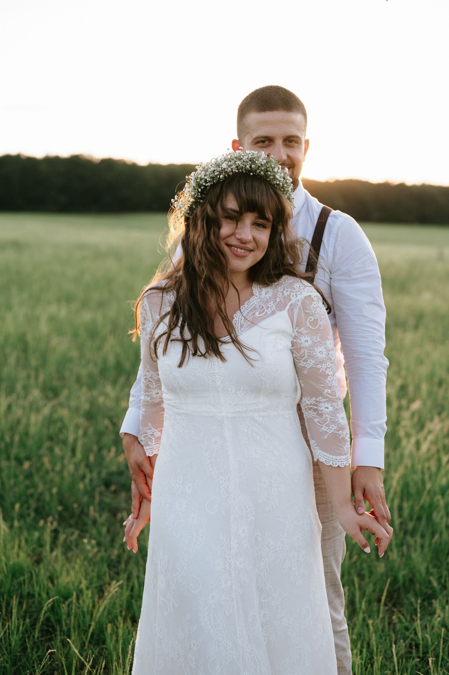 A romantic wedding portrait in a green field at sunset.