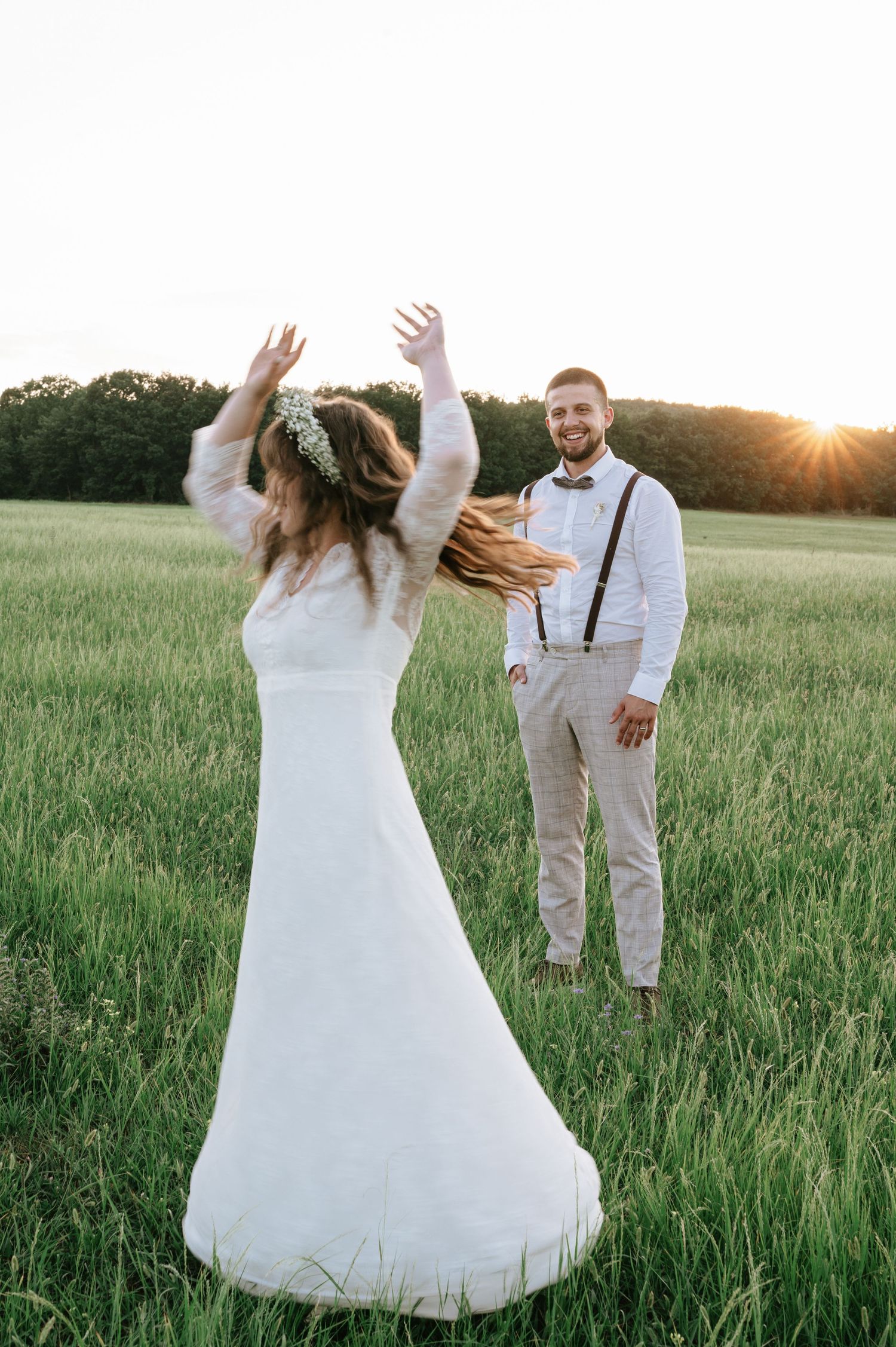 A couple shares playful moments in a grassy field during their wedding photoshoot at sunset.