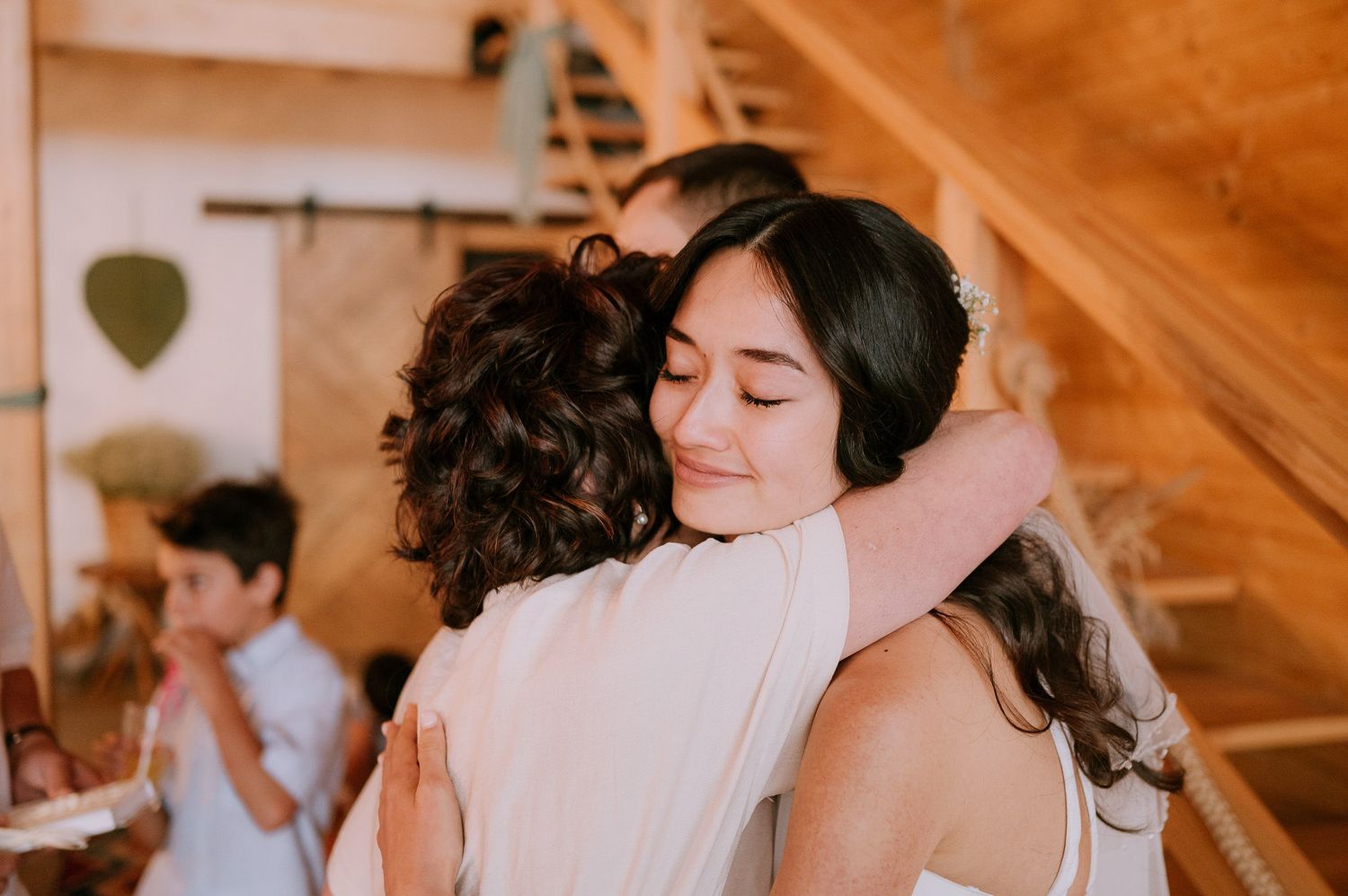 Two people share an emotional embrace during a wedding celebration in a warmly lit indoor venue.