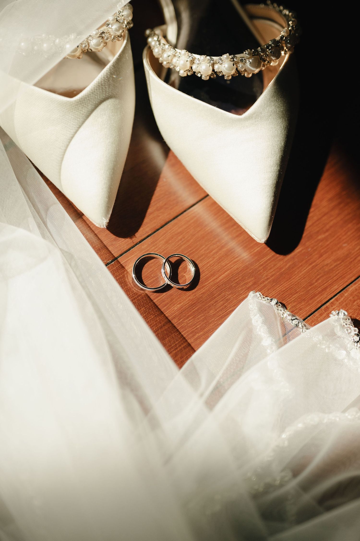 Wedding rings and bridal accessories arranged on wooden surface with soft light.