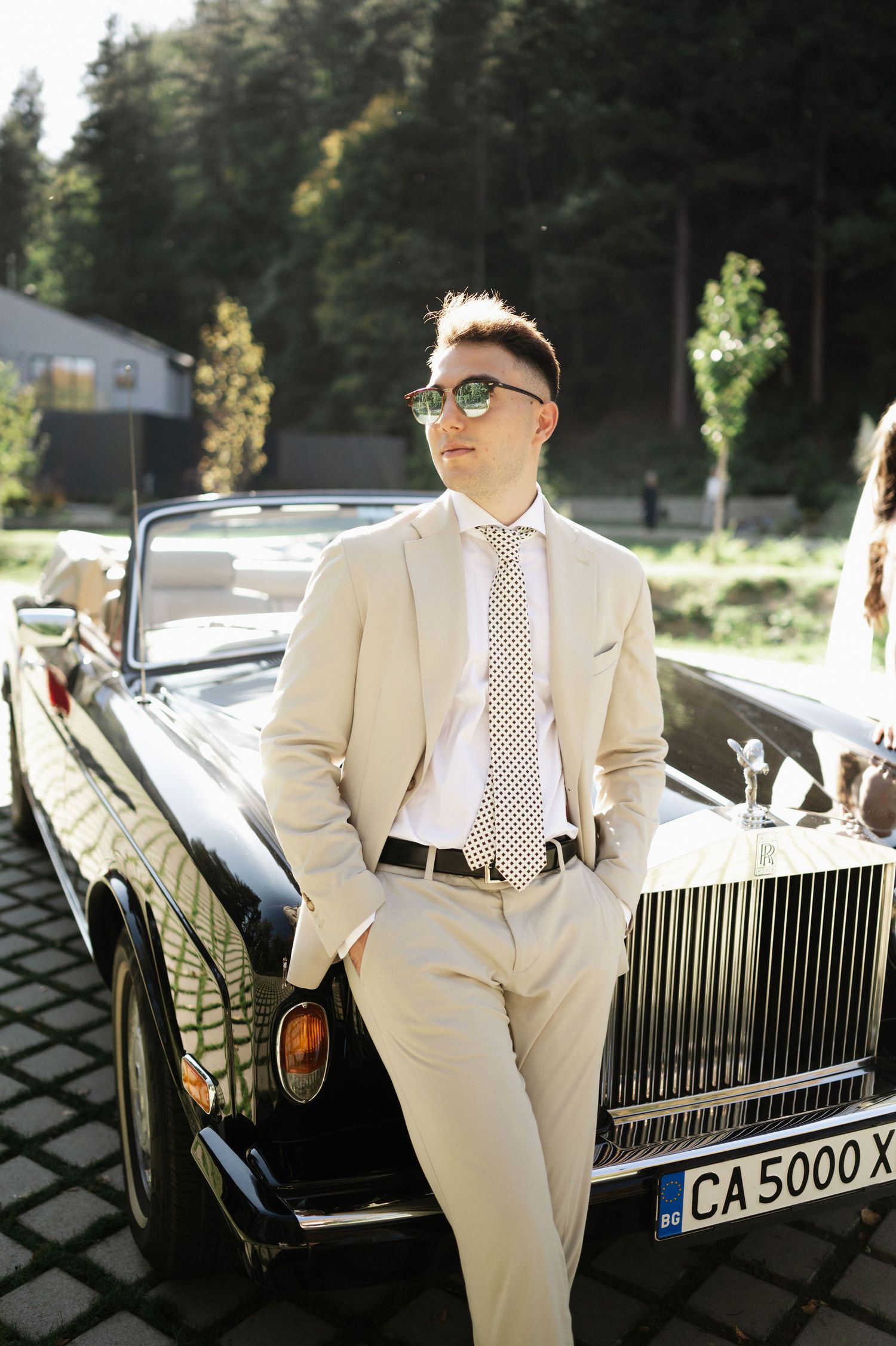 Fashion-forward portrait with vintage Rolls Royce against forest backdrop.