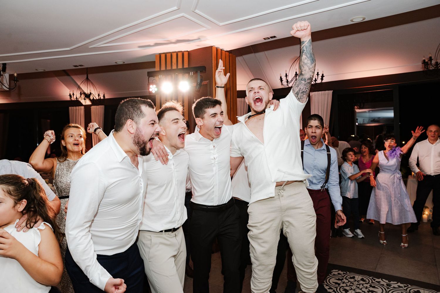 Large group dancing and having fun at an indoor wedding reception with white decor.