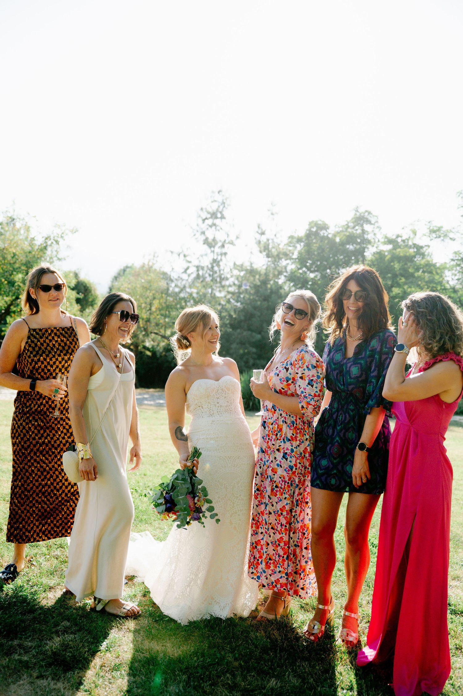 Wedding attendants in vibrant dresses laugh together during an outdoor photo session.