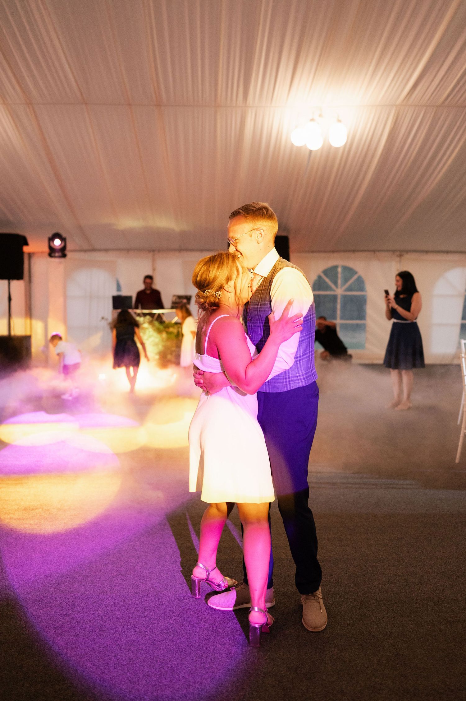 Purple lighting illuminates dancers on the dance floor at an evening wedding reception.