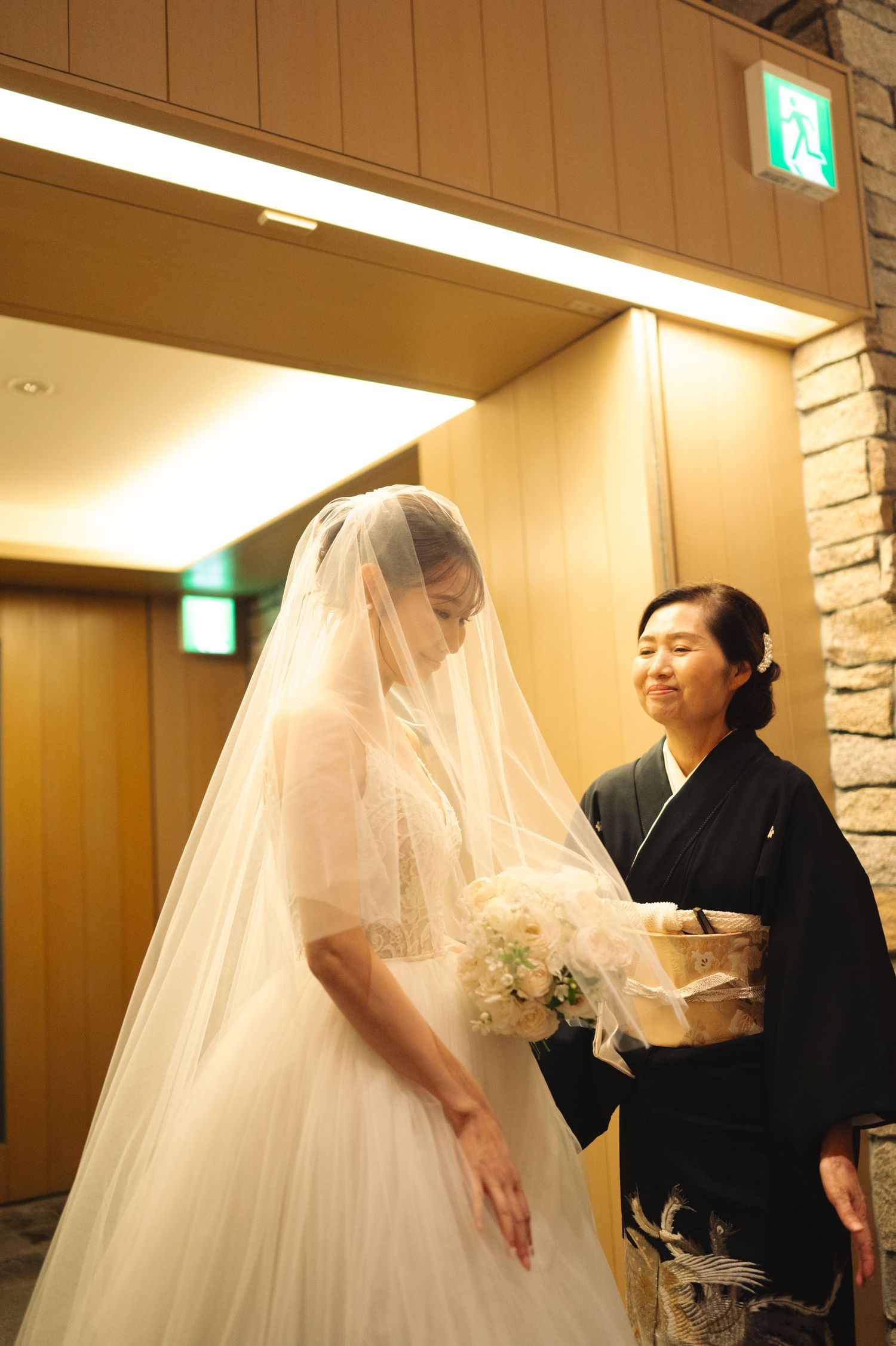 Final wedding dress adjustments being made in elegant venue with stone wall backdrop.