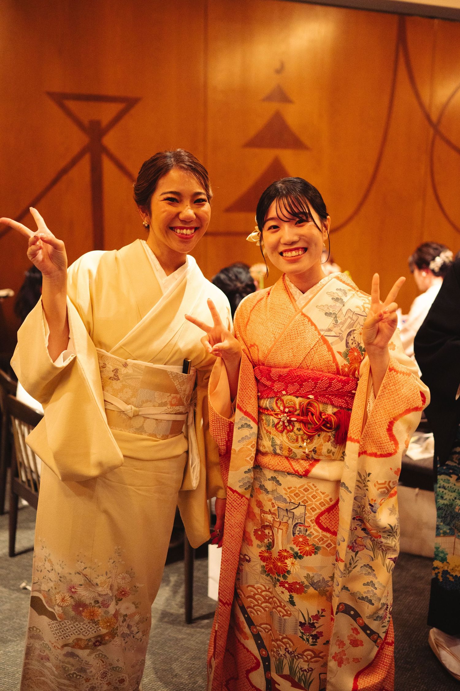 Group wearing ornate kimonos in white, orange and red poses together at formal gathering.