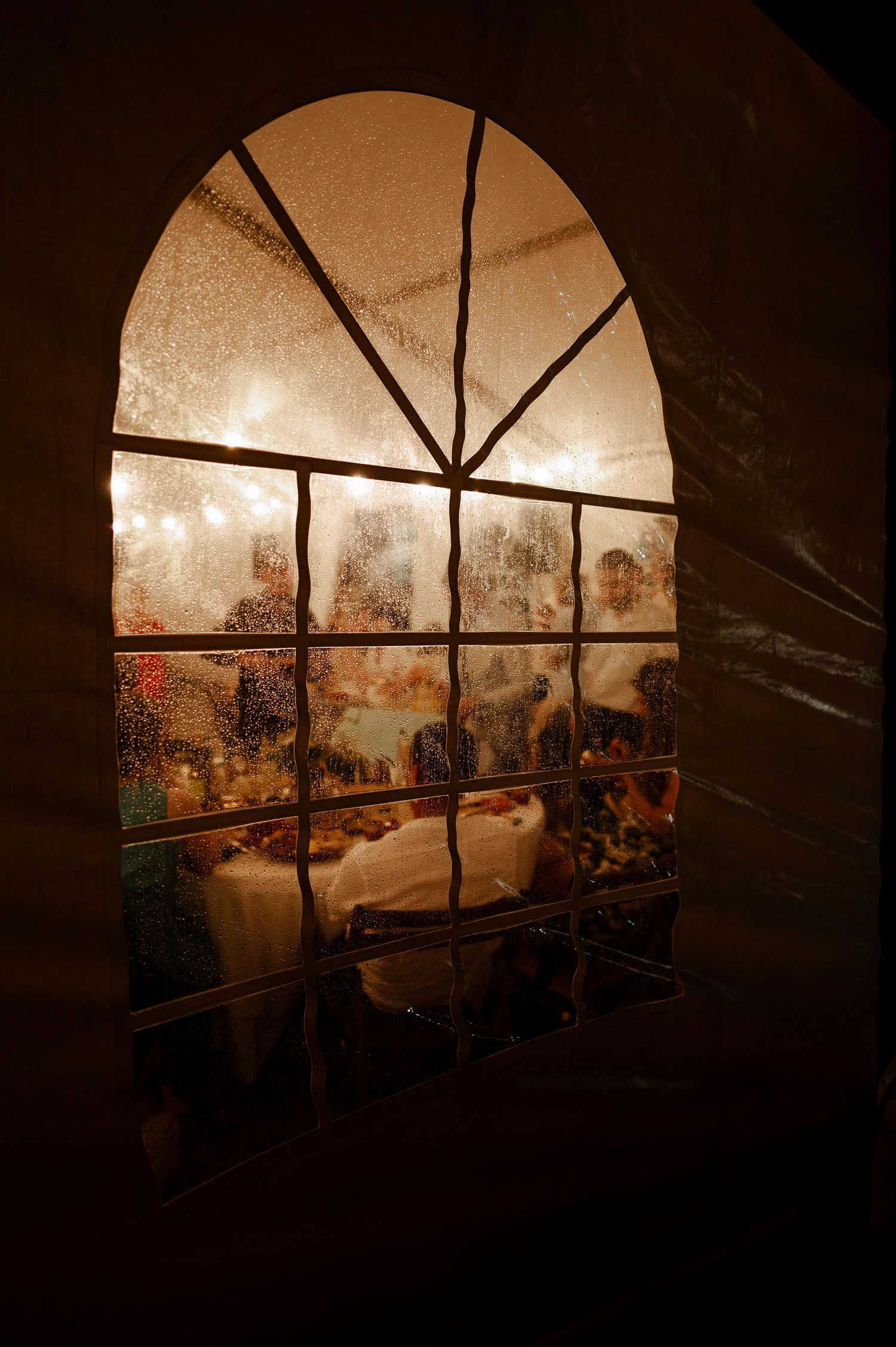 Atmospheric view through arched windows showing warm lighting and party silhouettes.