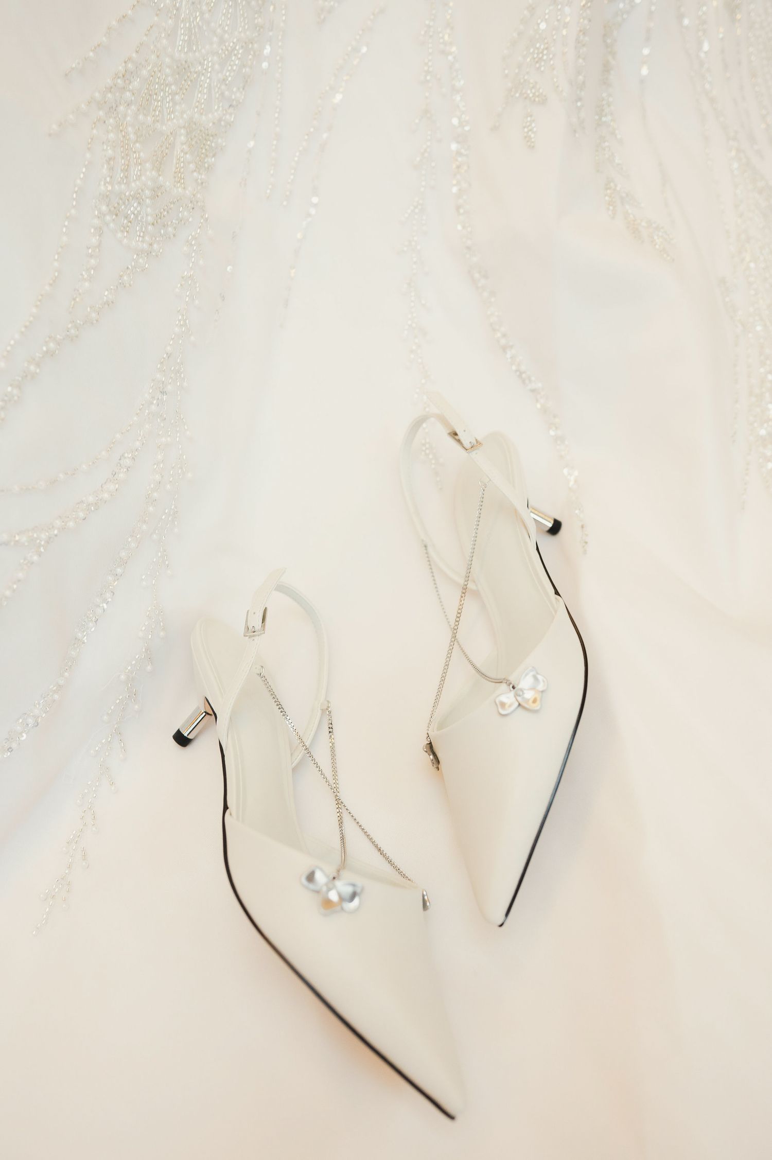 Delicate white bridal flip flops with small floral embellishments on a light marble background.