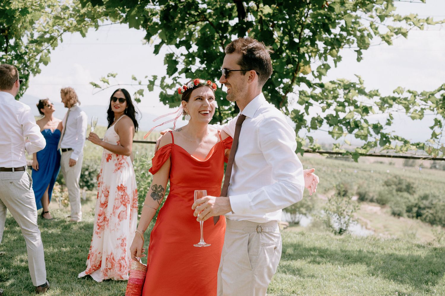 Outdoor wedding celebration with guests mingling under green trees.