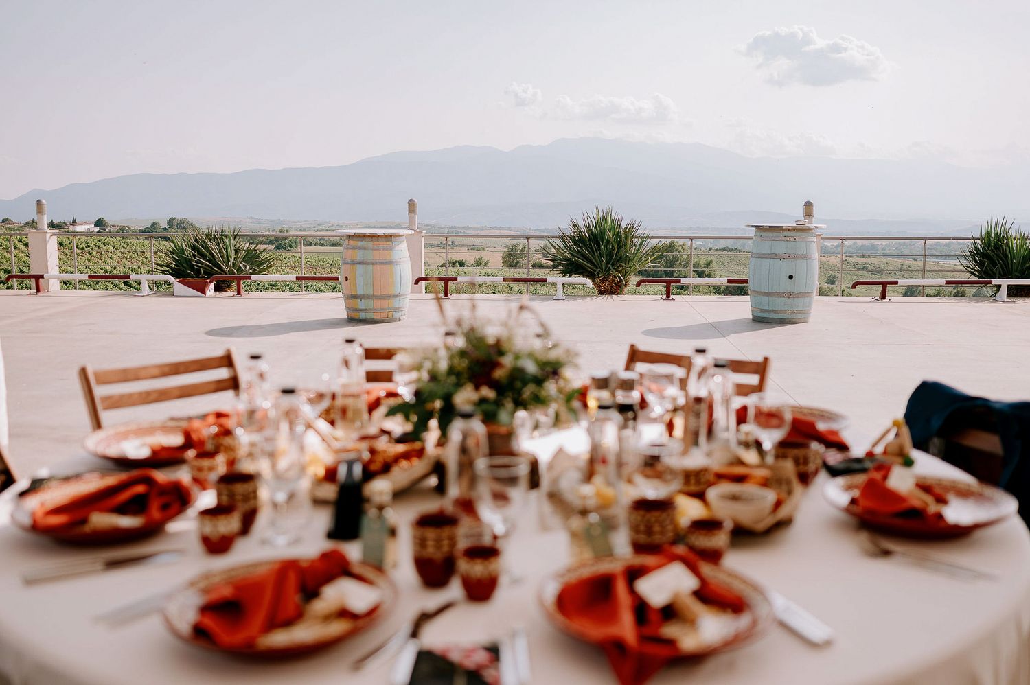 An elegant outdoor wedding reception table set with coral-colored plates and floral centerpieces against a scenic backdrop.
