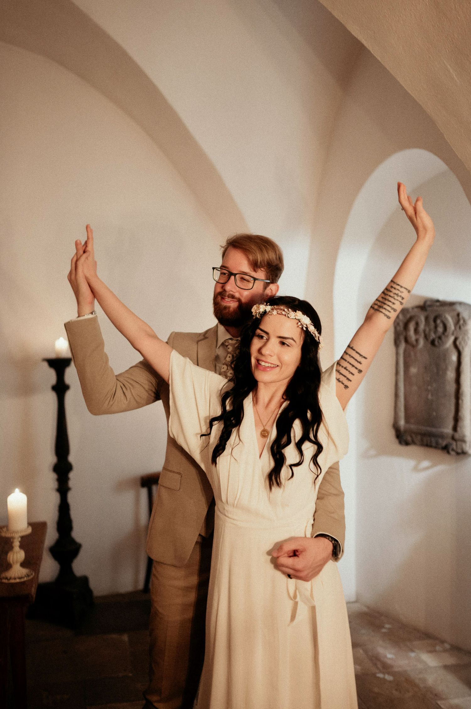 People raising their hands in celebration inside a white-walled room with candlelit ambiance.