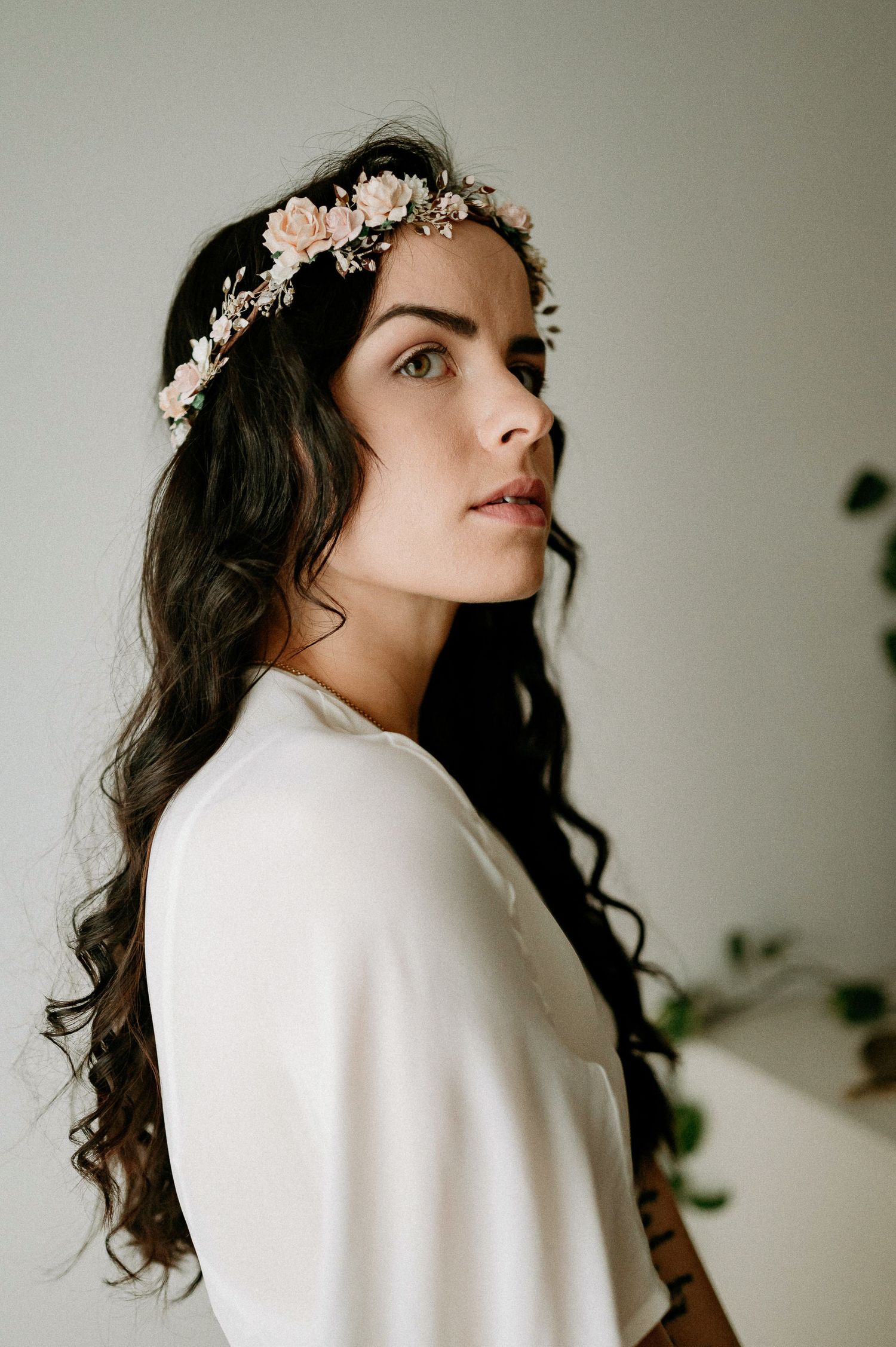Side profile portrait in white clothing with a floral crown against neutral backdrop.