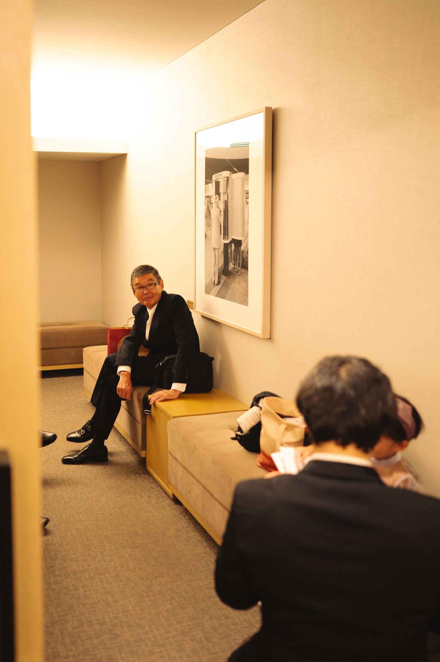 People in formal attire seated in a hallway during an event.