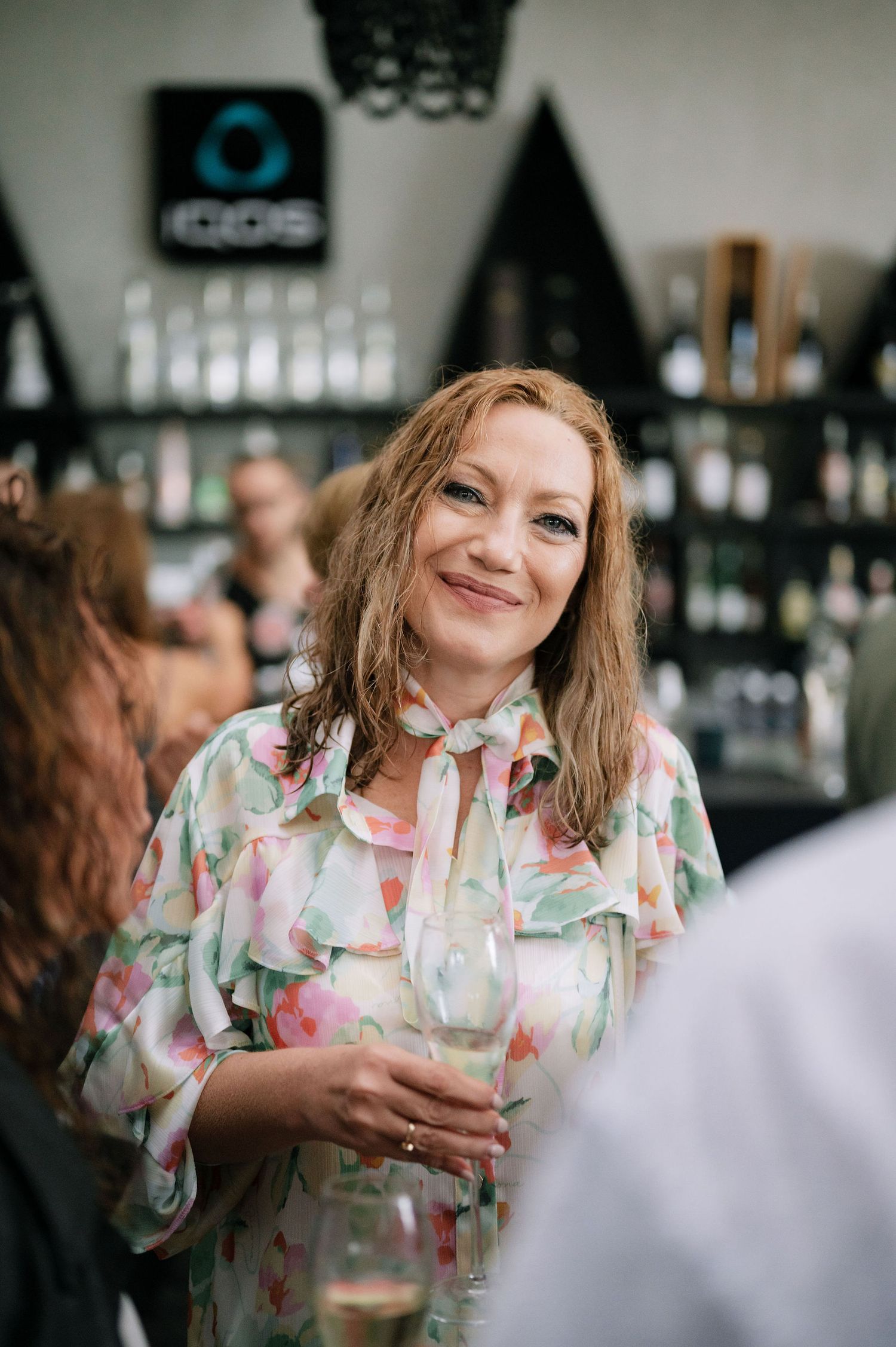 A guest in a floral print dress enjoys drinks at a bar during a celebration.