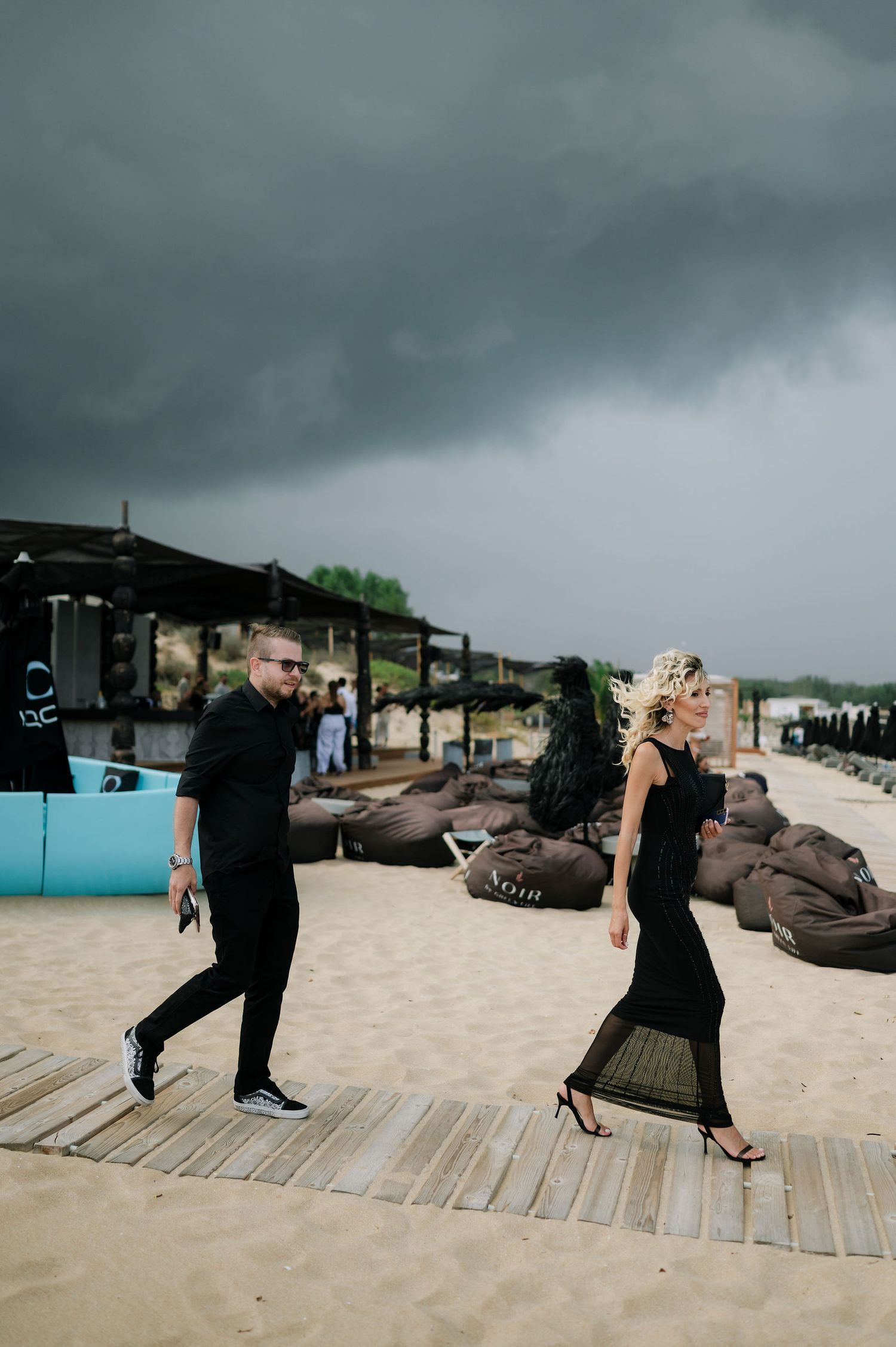 Guests walking along a wooden boardwalk on a stormy beach day.