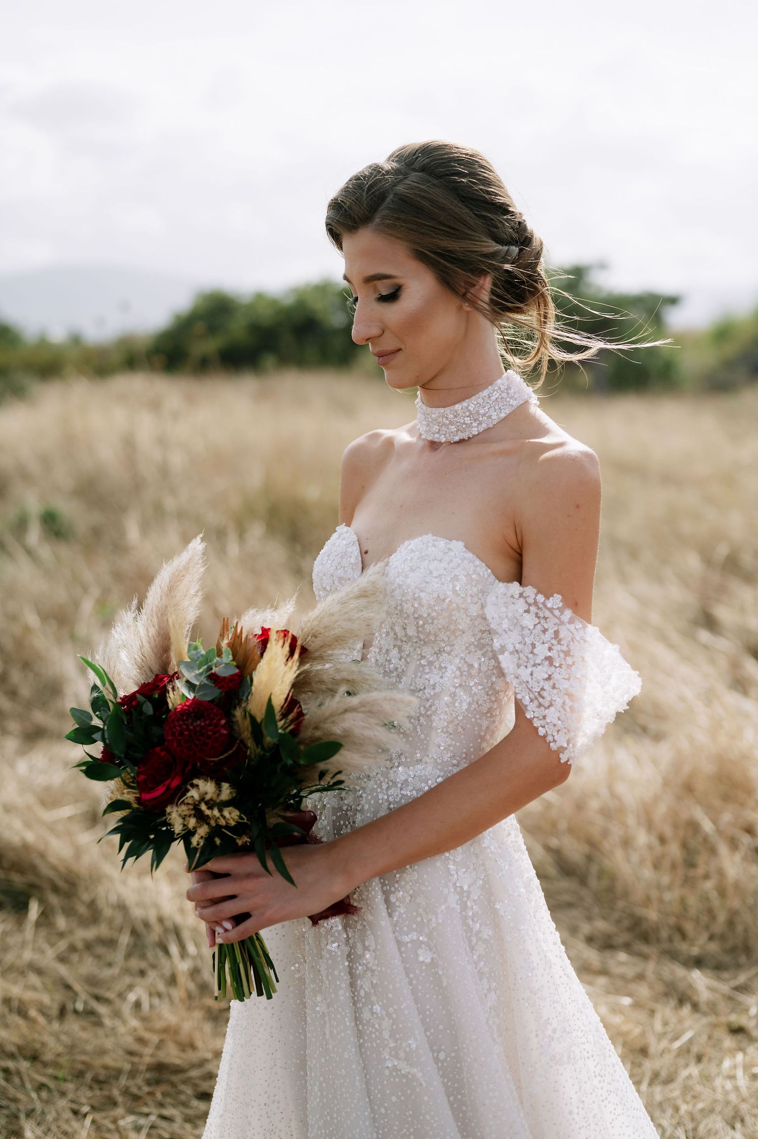 Close-up shot of a bride's off-shoulder wedding dress with delicate lace details and burgundy floral bouquet.