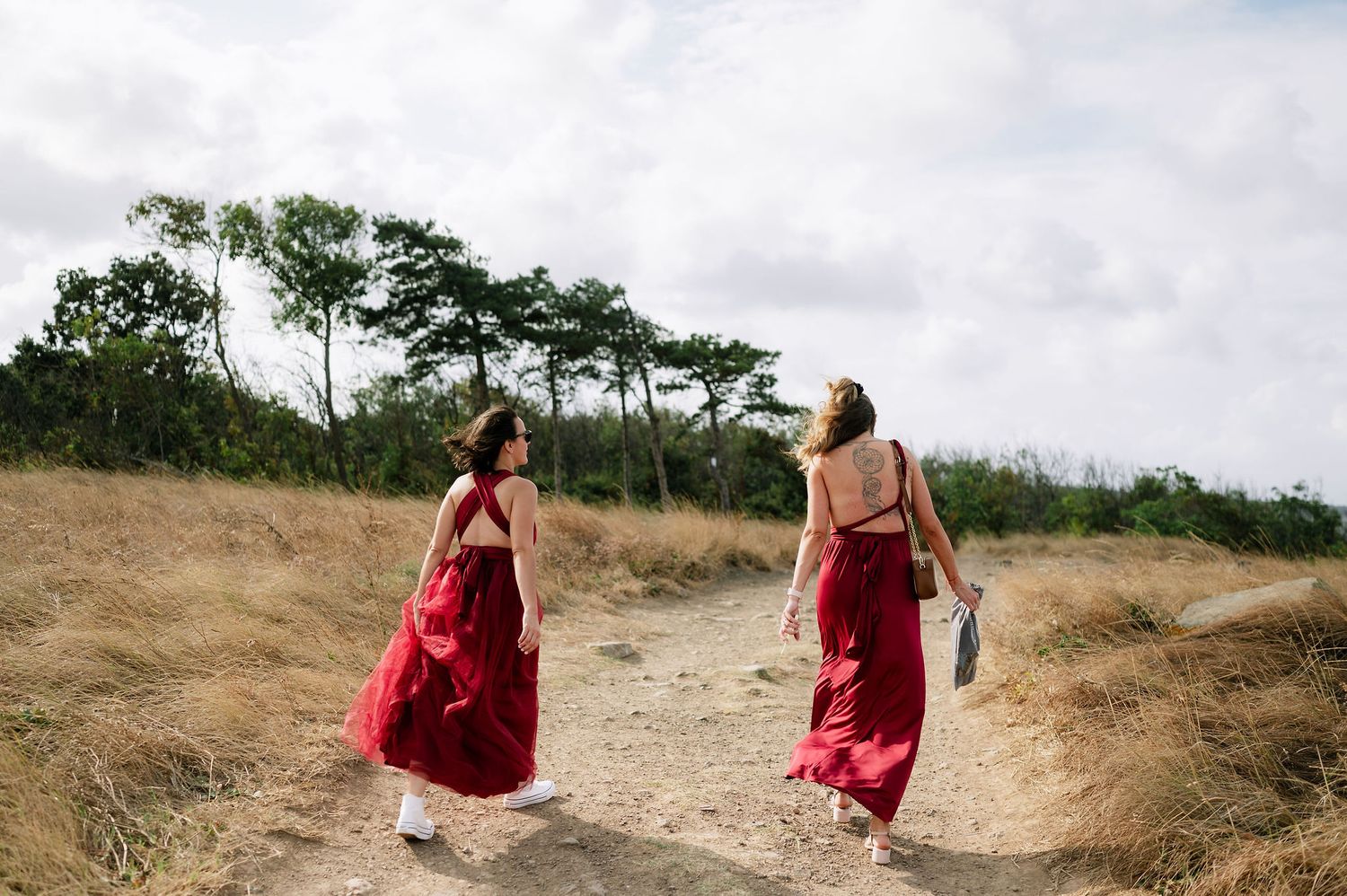 People in red dresses walking along a sandy path near the ocean.