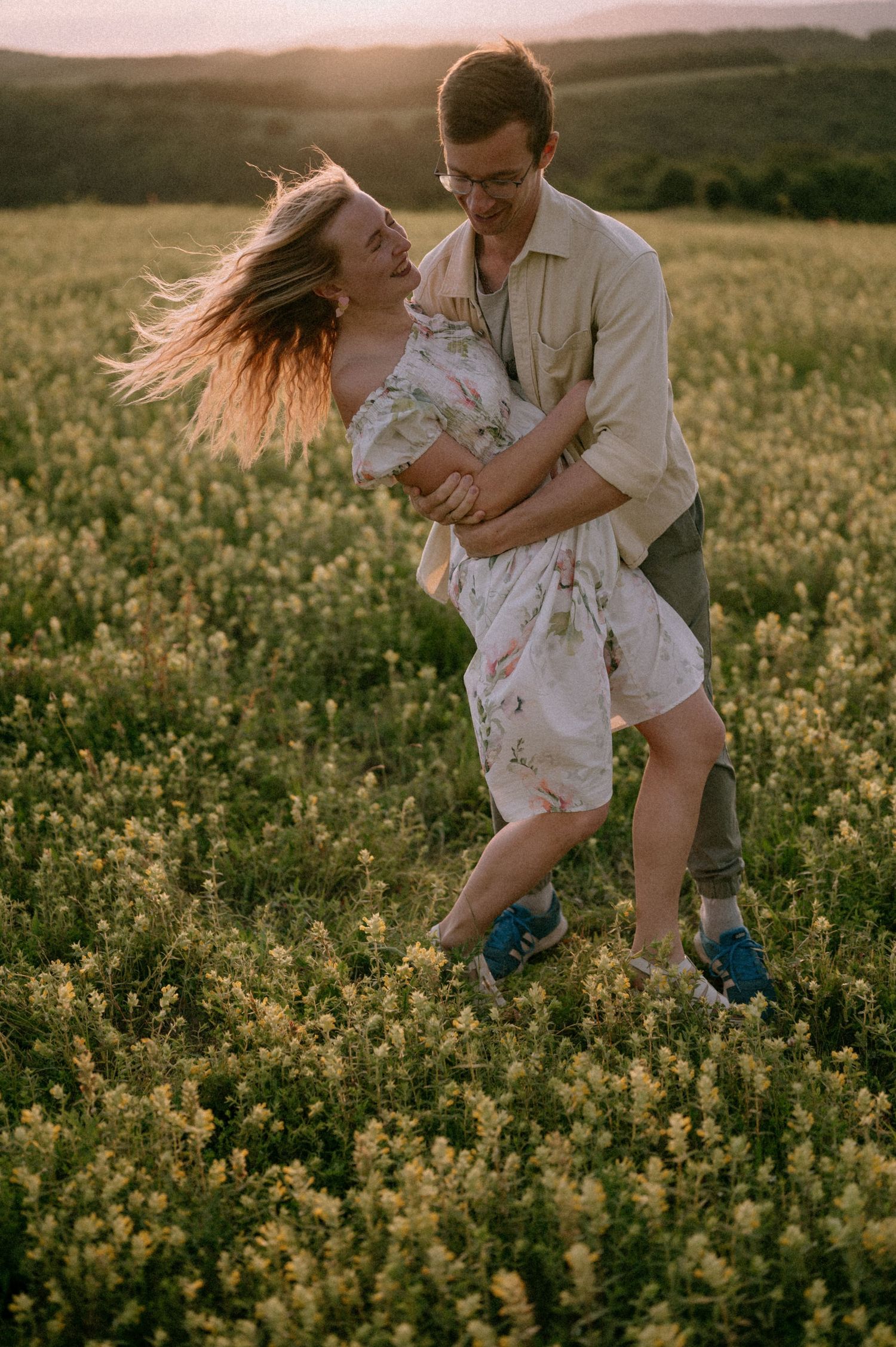 A playful couple dances through a blooming yellow canola field at sunset.