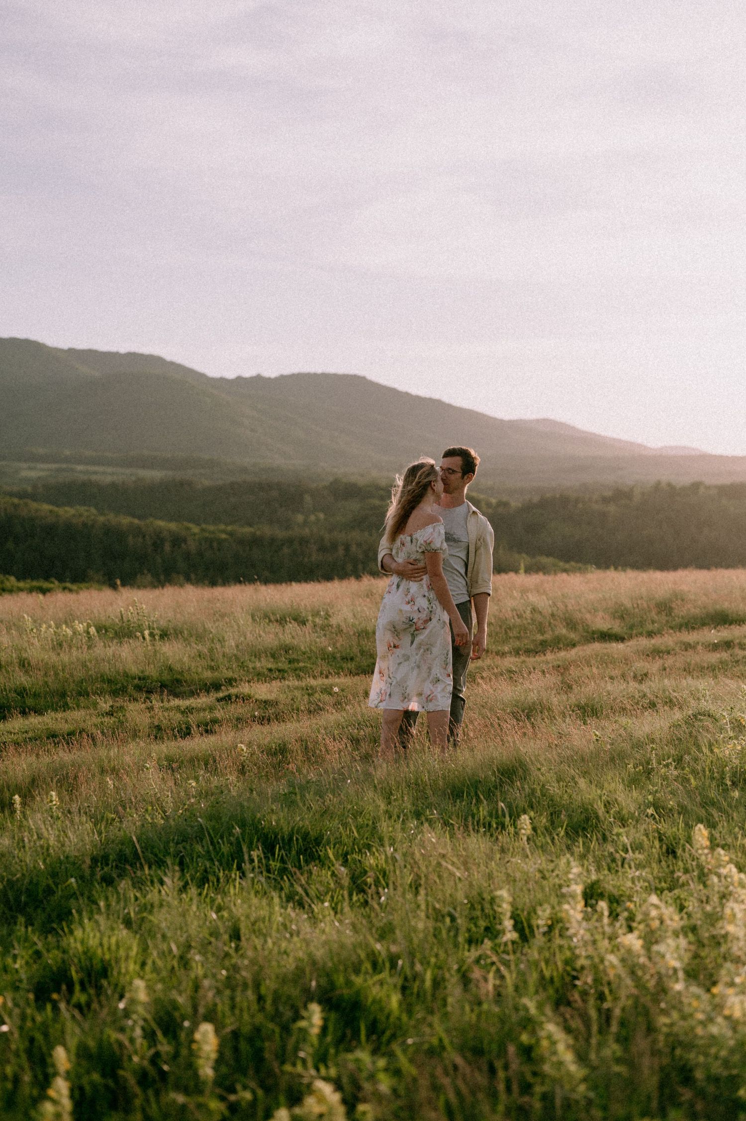 Romantic couple embracing in a mountain meadow during golden hour.