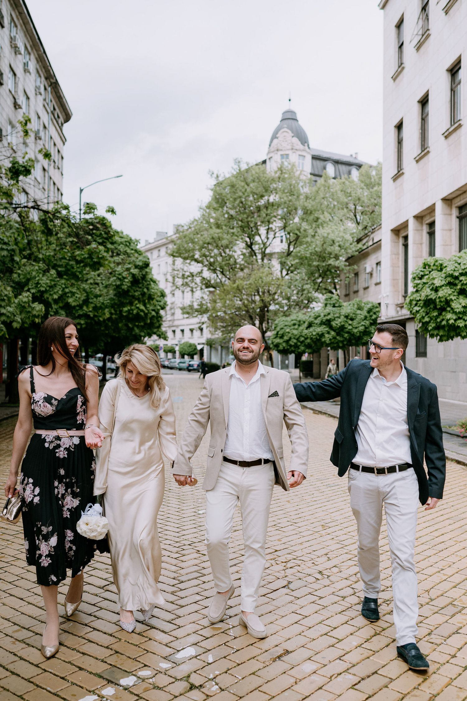 Group walking together in coordinated white and beige outfits on a cobblestone street.