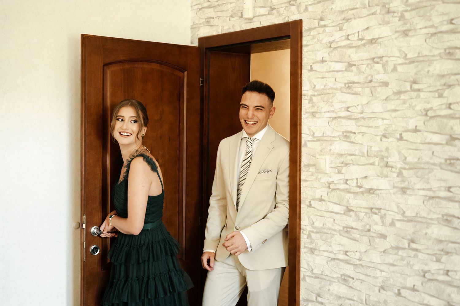 A couple in formal wear share a playful moment by a doorway.