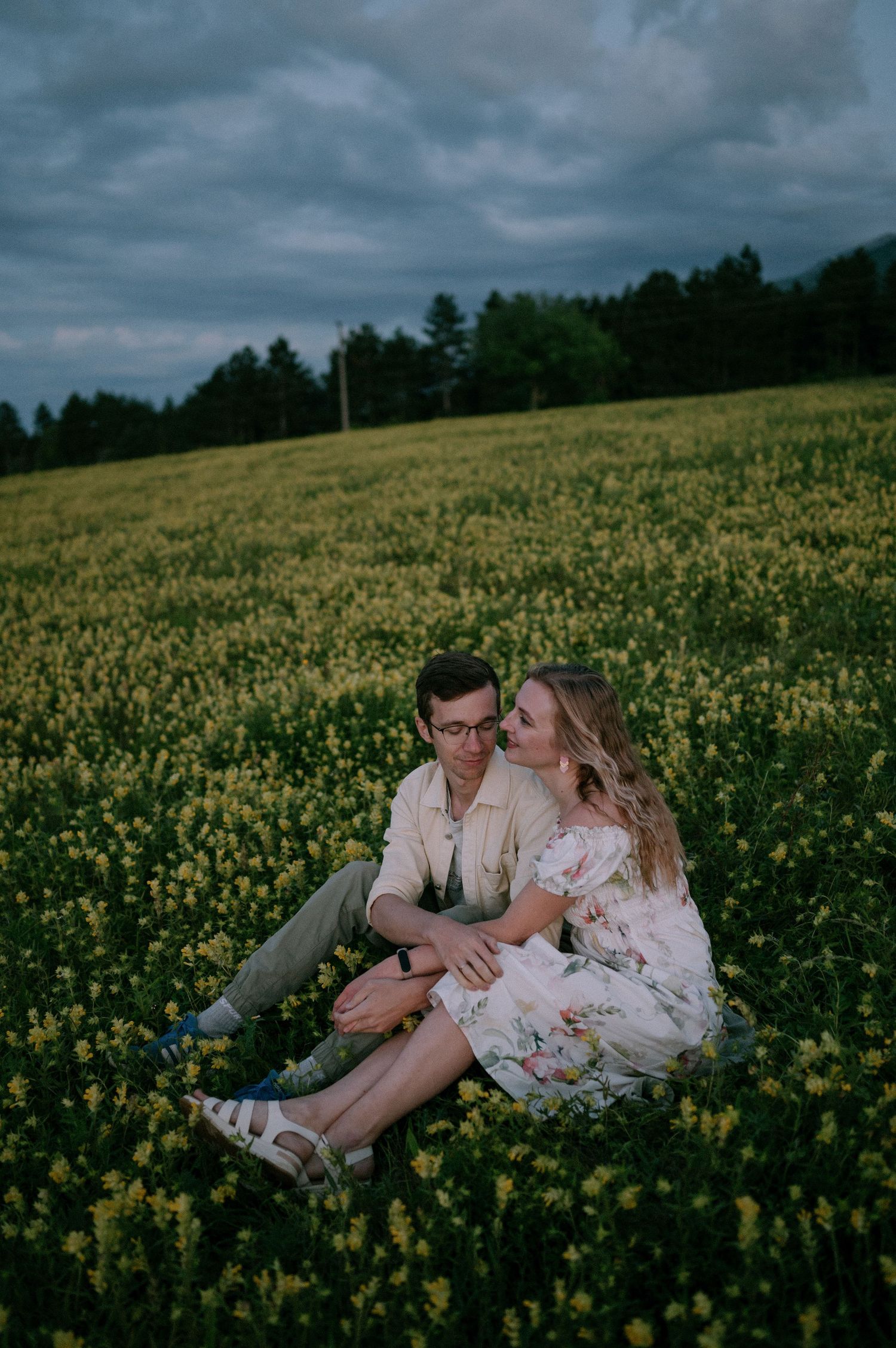 A couple embraces while resting in a vast field of yellow wildflowers during golden hour.