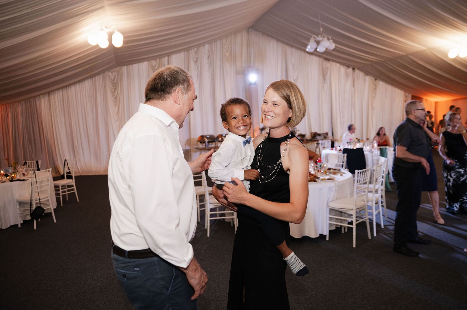 People dancing and socializing at an indoor wedding reception under white tent draping and lighting.