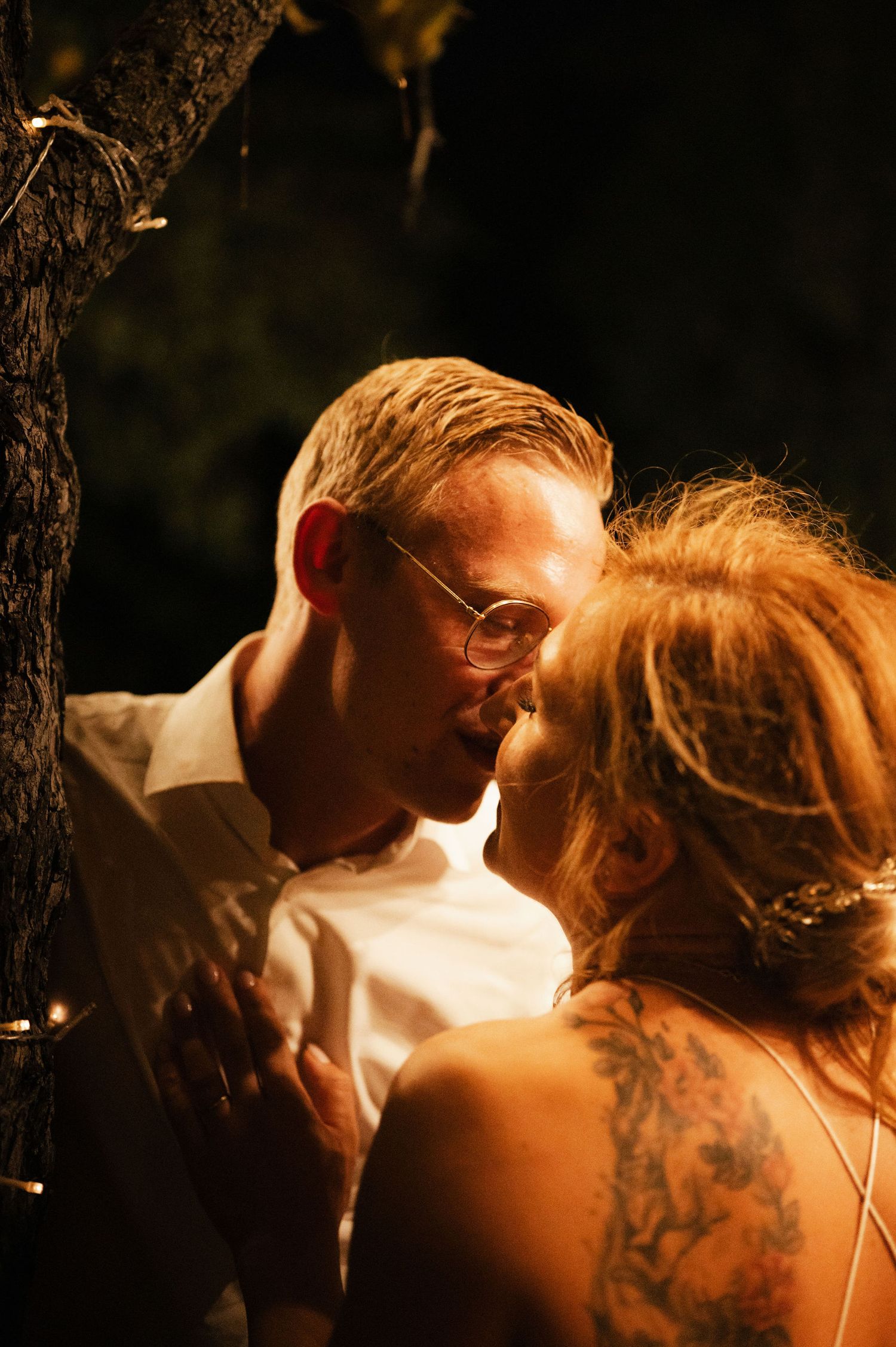 A romantic couple shares an intimate moment in warm backlit lighting at sunset.