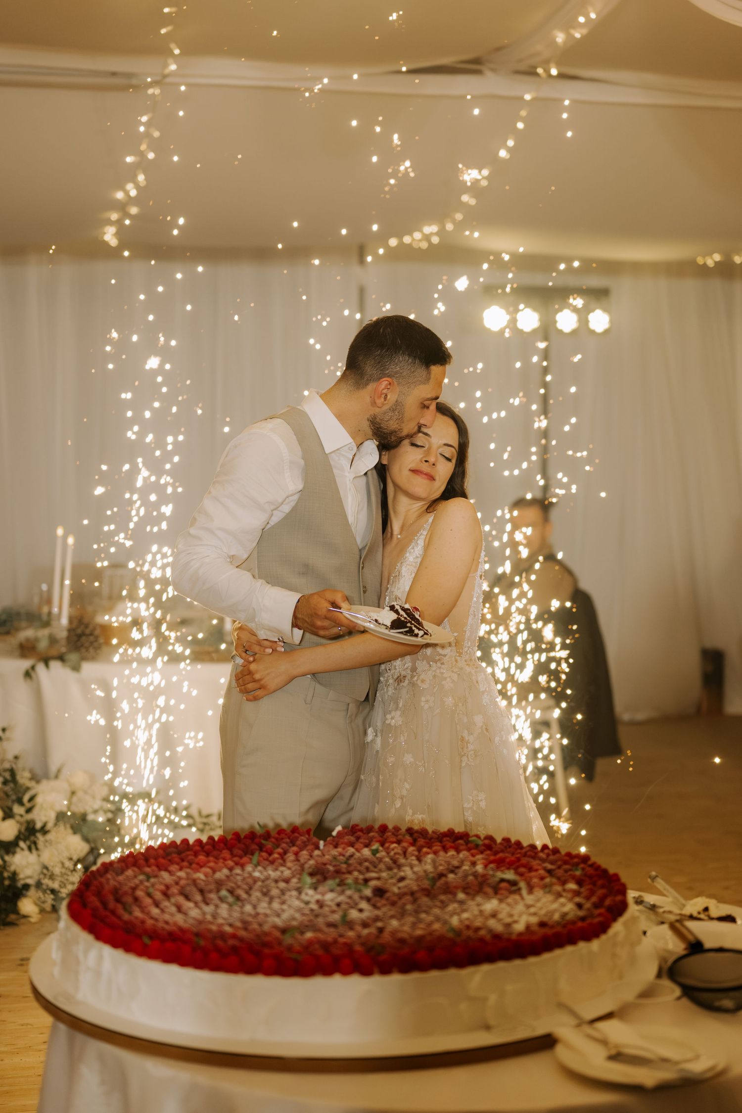 Bride and groom cutting wedding cake surrounded by sparkling fireworks in elegant reception venue.