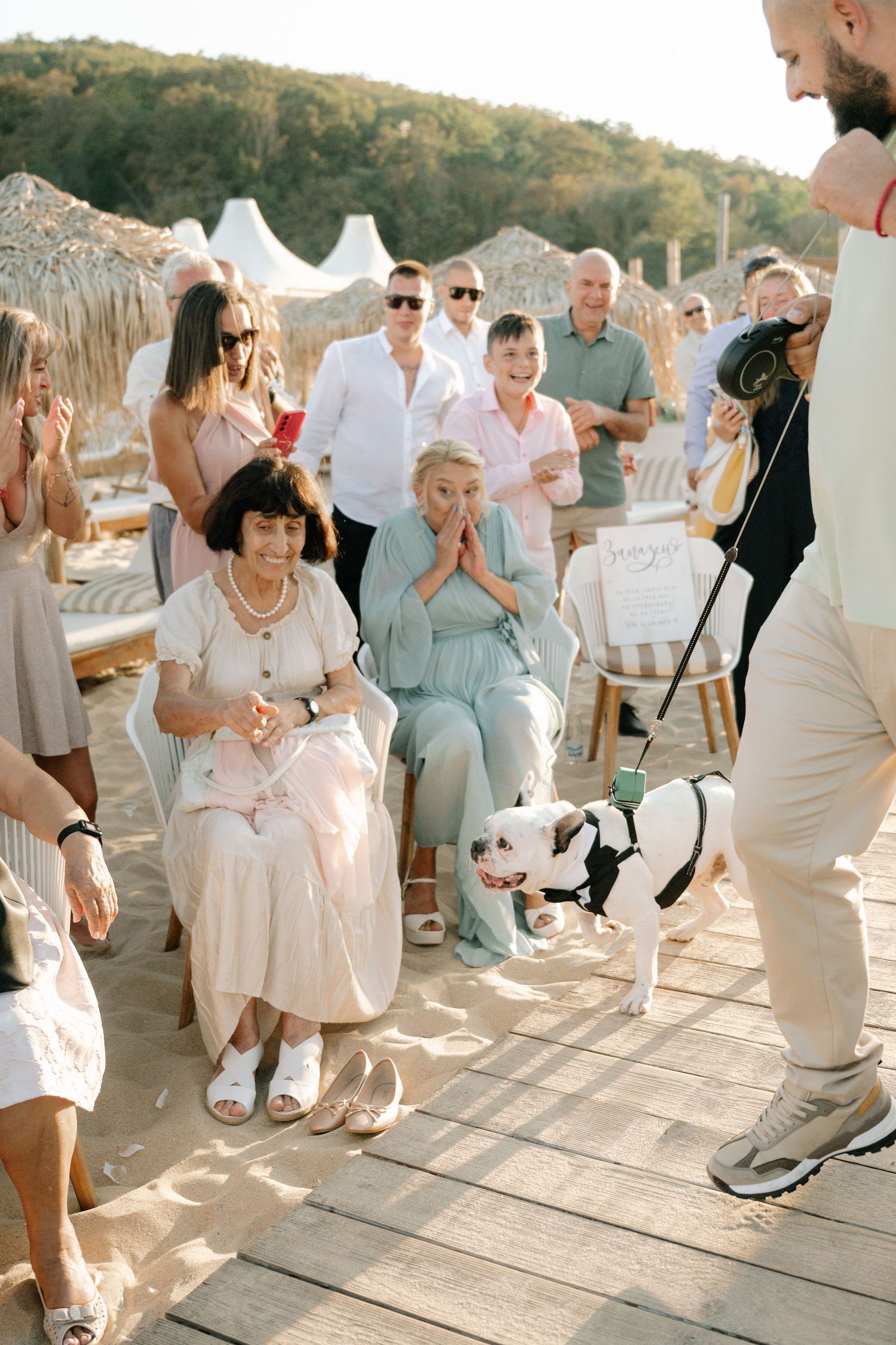 Wedding guests dance and celebrate on a wooden deck during a sunset reception.