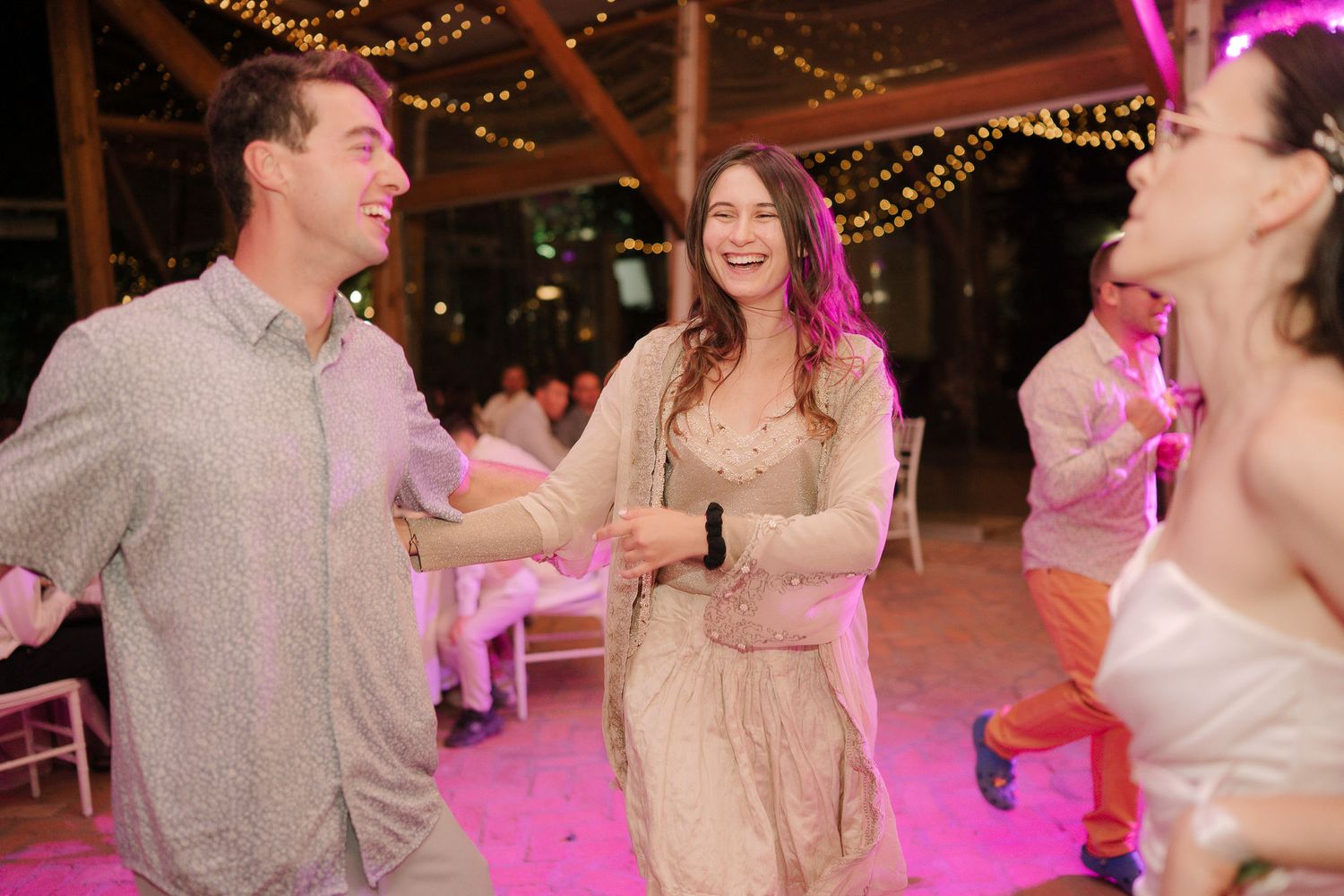 Couples dancing together at an evening reception with pink lighting and string lights creating a romantic atmosphere.