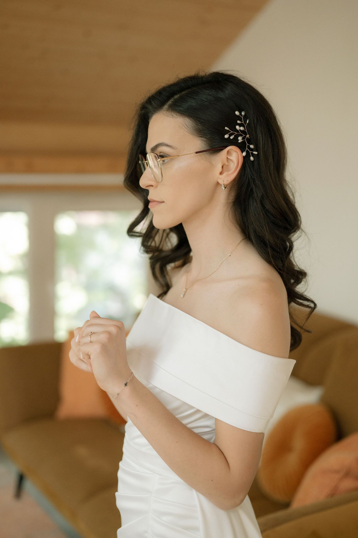 A bride in a white strapless dress smiles and adjusts her hair during wedding preparations.