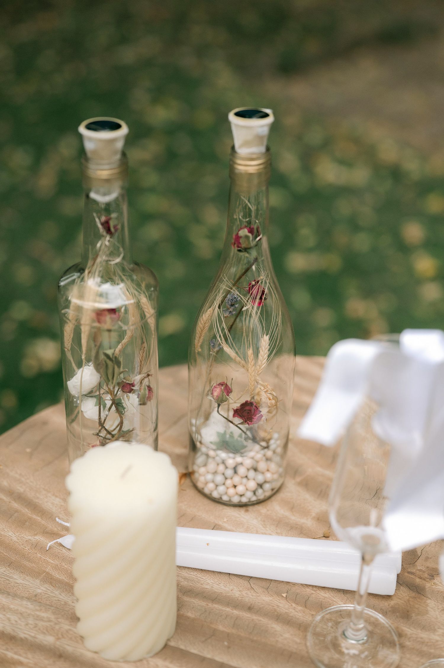 Decorative glass bottles with dried flowers and candles arranged on a rustic surface for an elegant event setting.