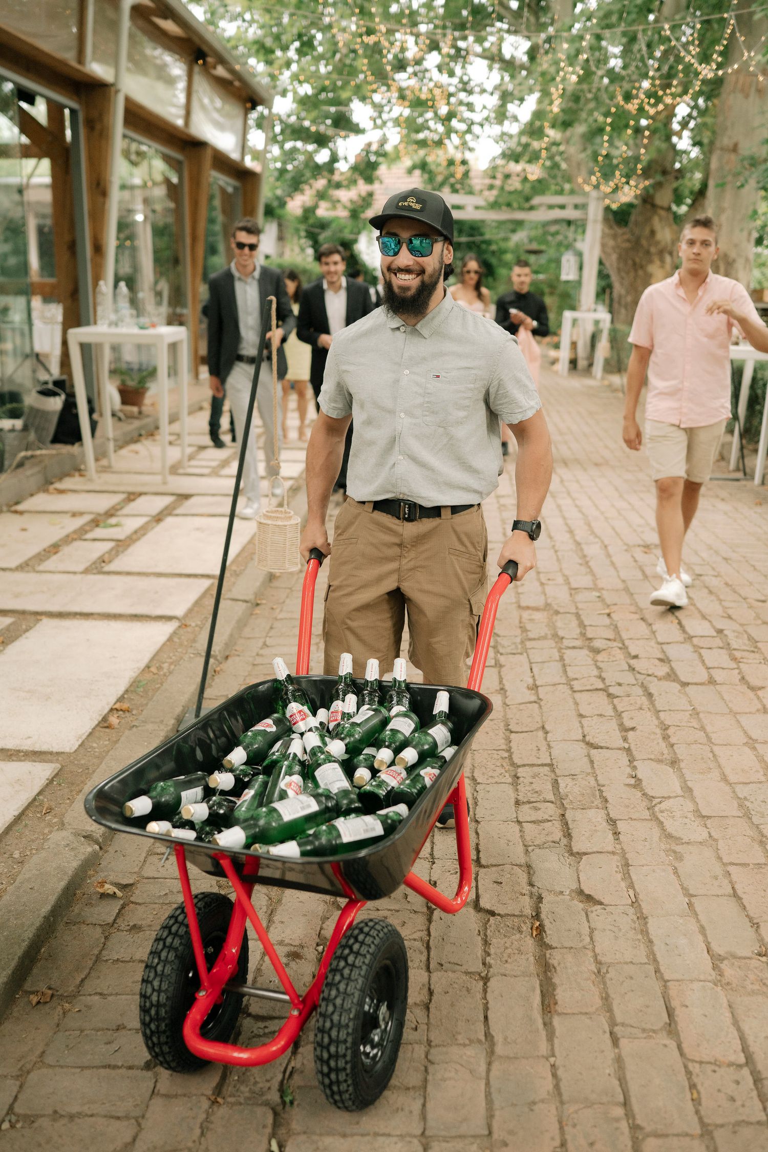 A sequence showing a wheelbarrow full of beer bottles being transported down a brick paved street.