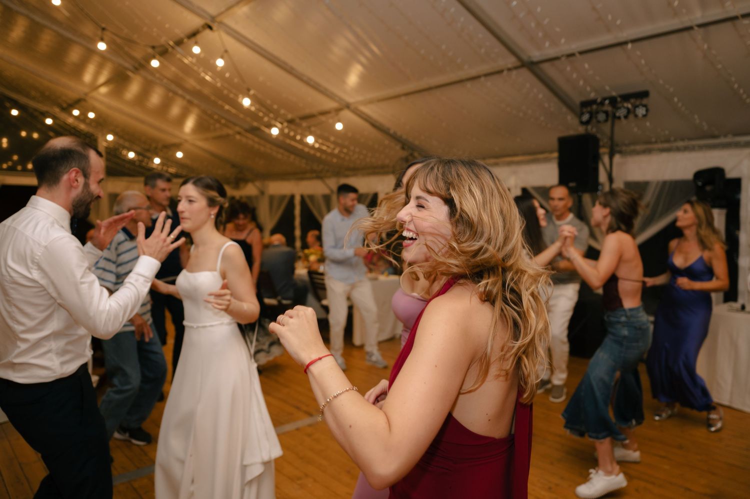 Couples dance together at an evening wedding reception in a warmly lit tent venue.
