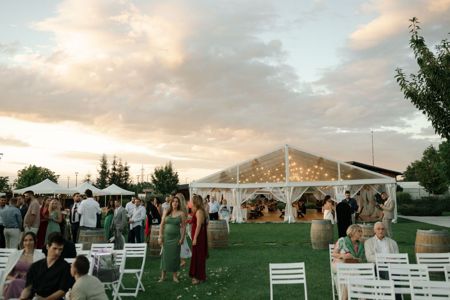 A wedding ceremony setup under a white tent with elegant chairs and decor at sunset.
