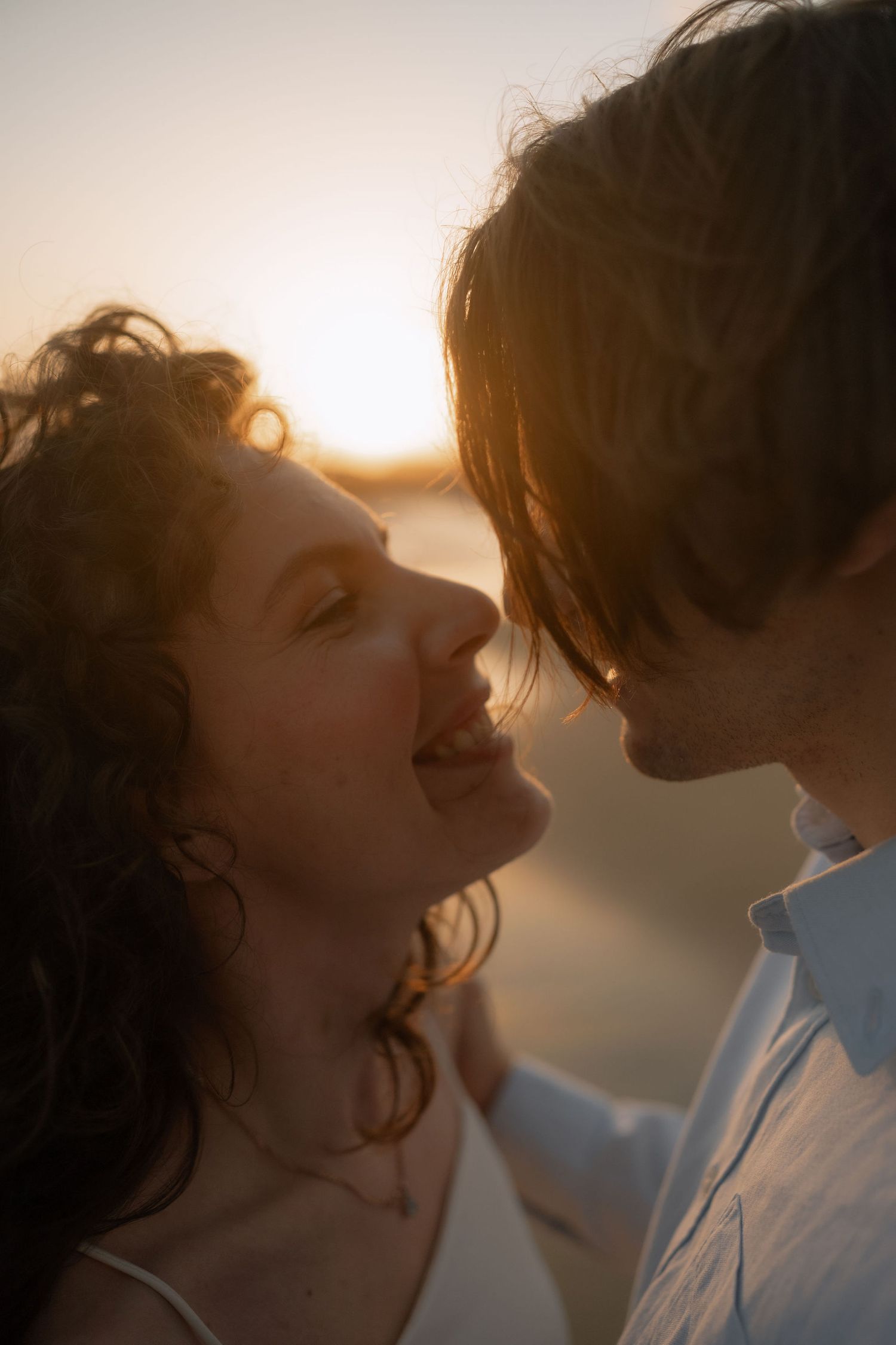 Romantic couple sharing a tender moment at golden hour sunset, smiling and leaning close together outdoors.