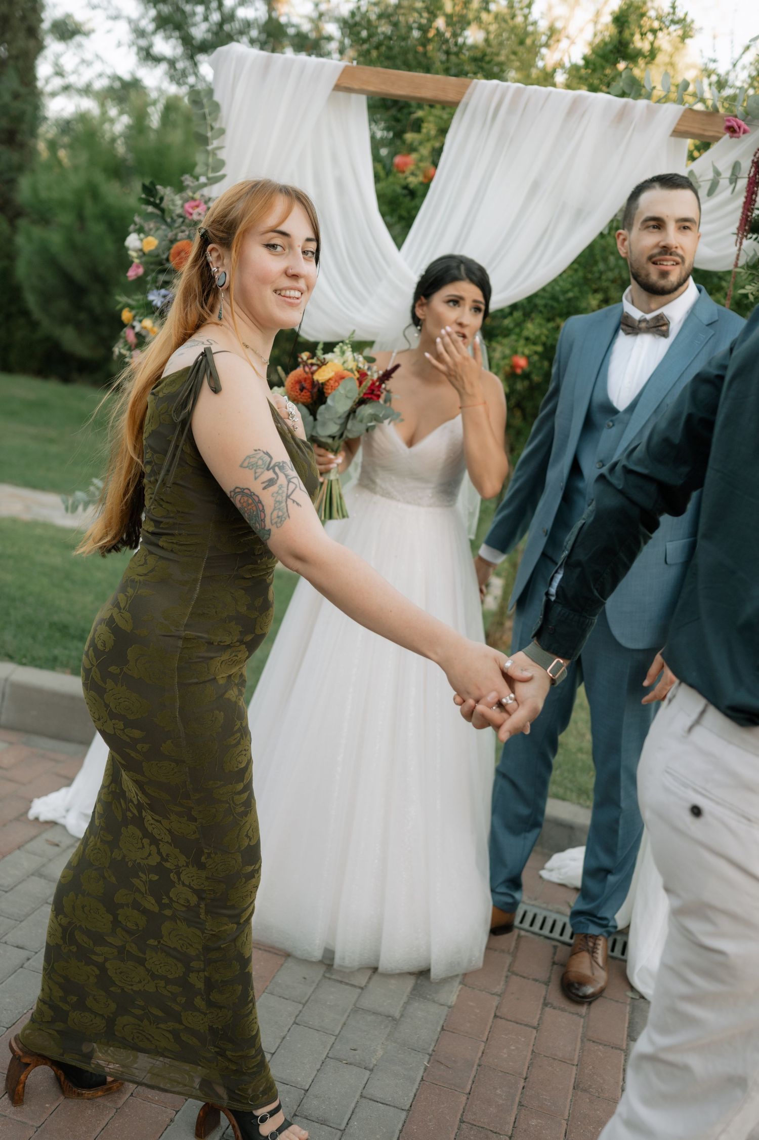Wedding guests dance and celebrate on an outdoor patio with white drapes and floral decorations in the background.