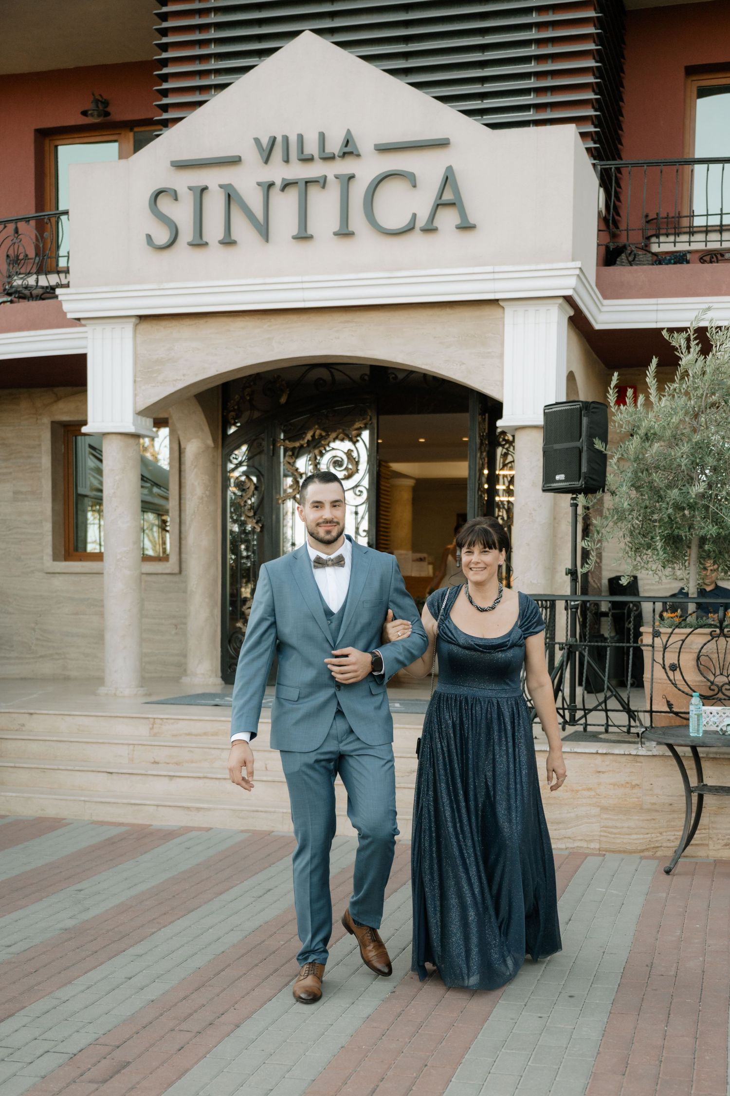 A couple in formal attire walking together on a wooden deck outside Villa Sintica.