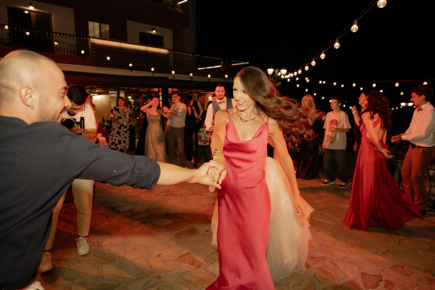 People dancing at a nighttime outdoor celebration with string lights creating a festive atmosphere.