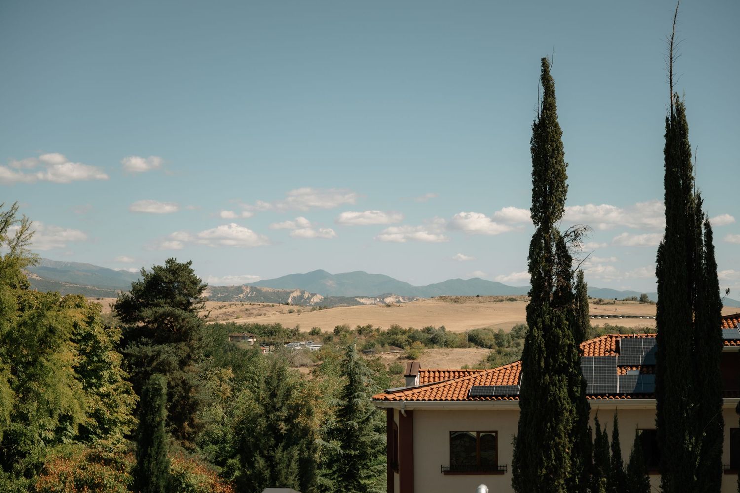 Scenic Tuscan countryside landscape with rolling hills, cypress trees, and traditional villa architecture under blue sky.