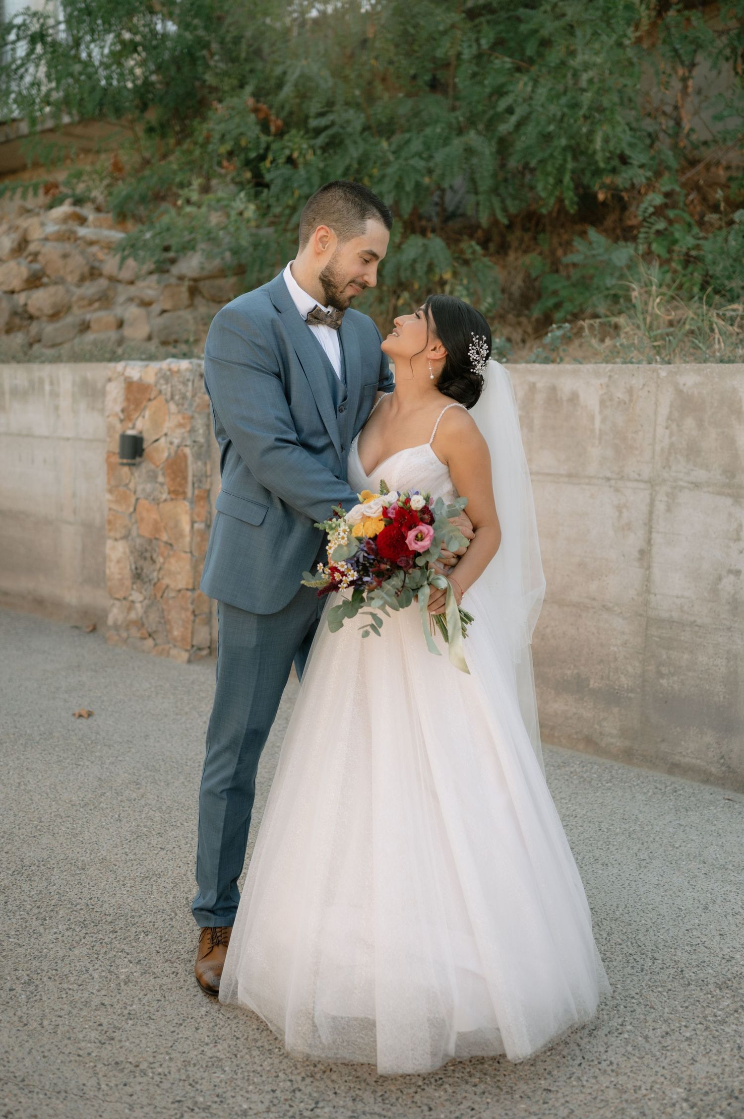 A romantic wedding couple shares an intimate moment on a stone path surrounded by greenery.