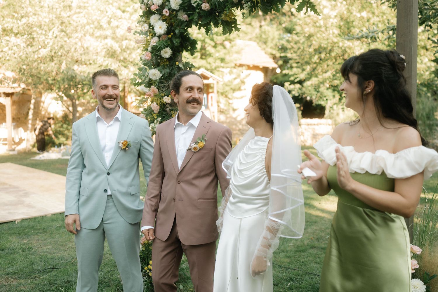 Wedding party gathered outdoors under trees during a summer garden celebration.