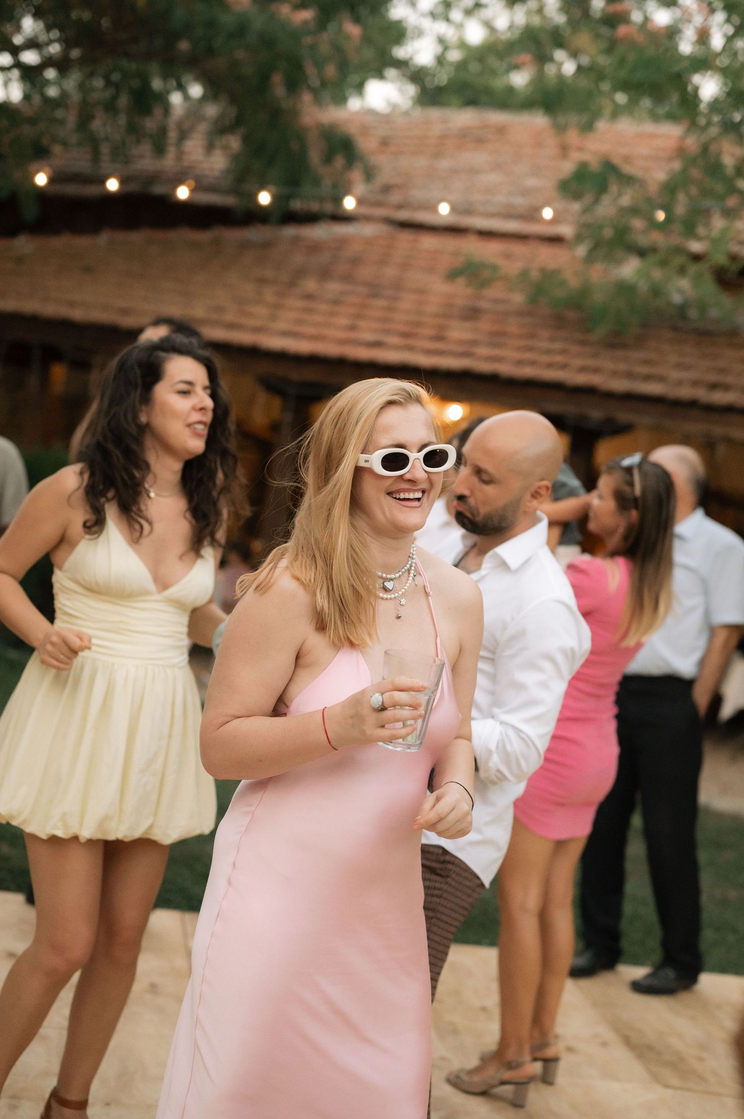 People dancing and celebrating at an outdoor party wearing light colored dresses and summer attire.