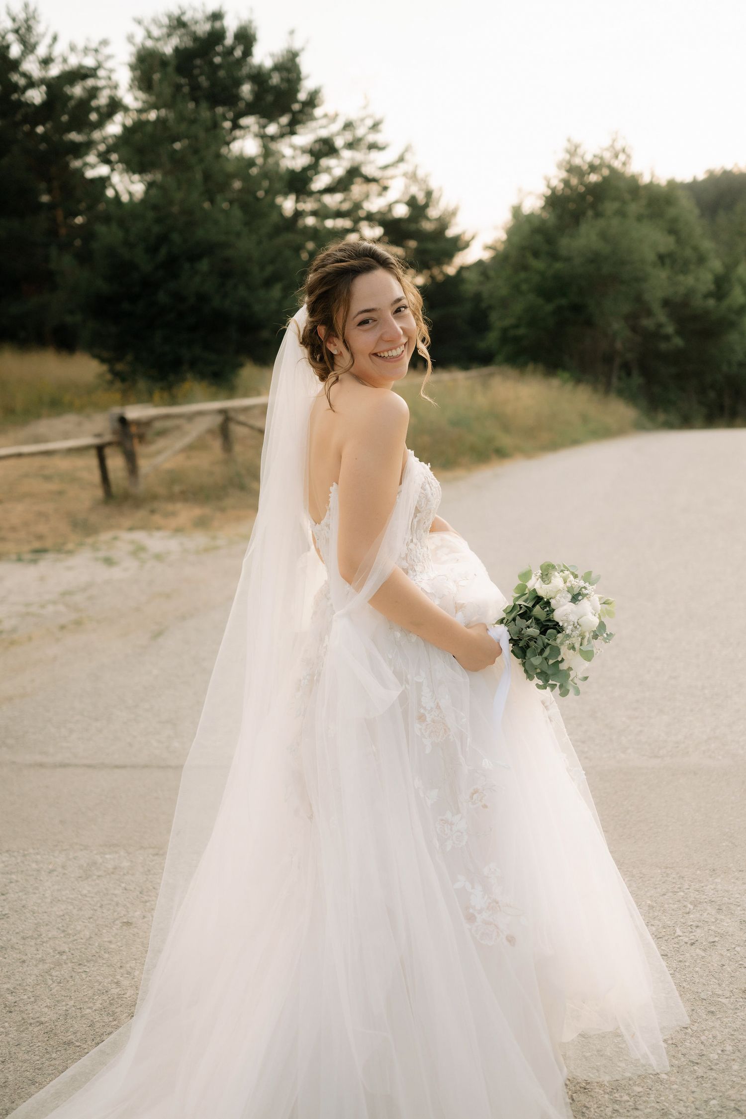 A flowing white wedding dress with a long veil captured in a series of romantic outdoor bridal portraits on a sandy path.