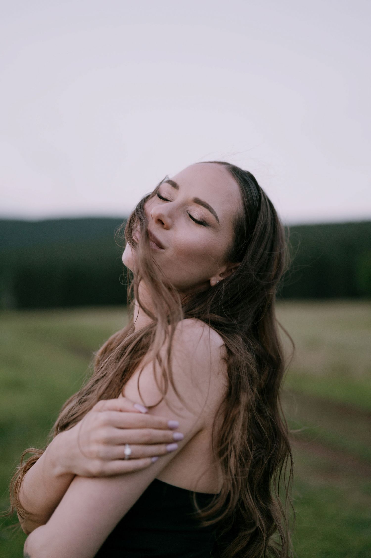 A person with closed eyes tilts their head back expressively against a moody outdoor landscape background.