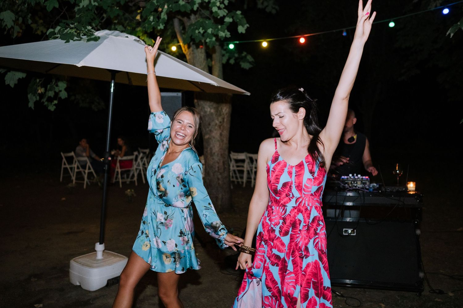 People dancing and having fun at a nighttime outdoor party in colorful tropical print dresses.