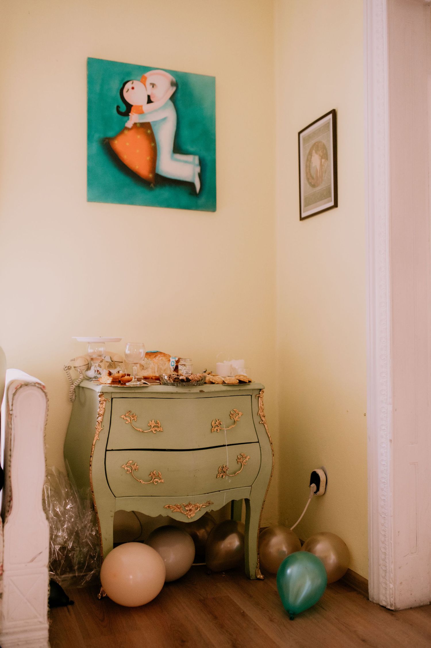 A vintage dresser with floral details sits against a white wall with teal artwork and decorative elements.