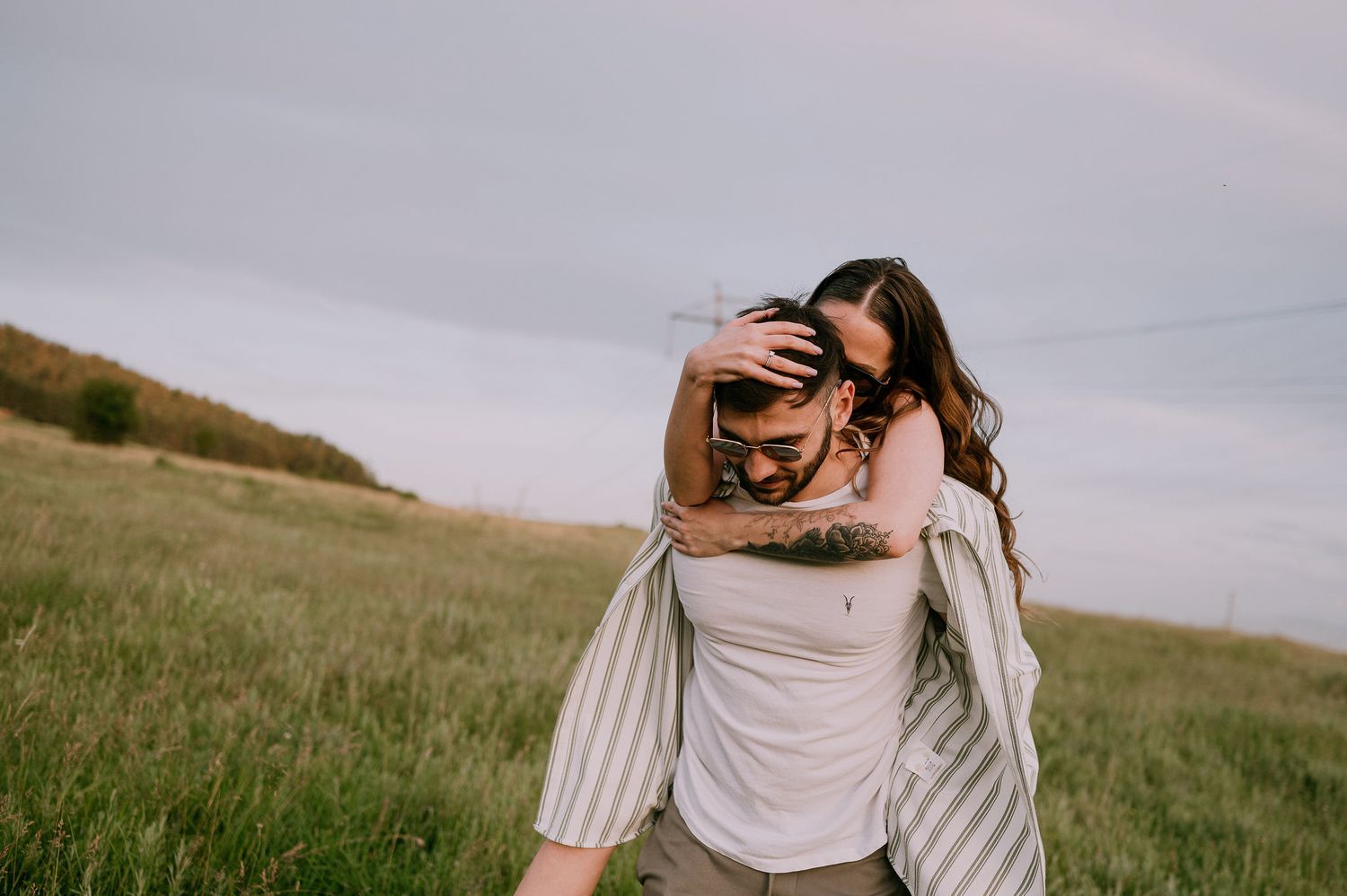 A couple embraces in a romantic moment on a grassy hillside during sunset.