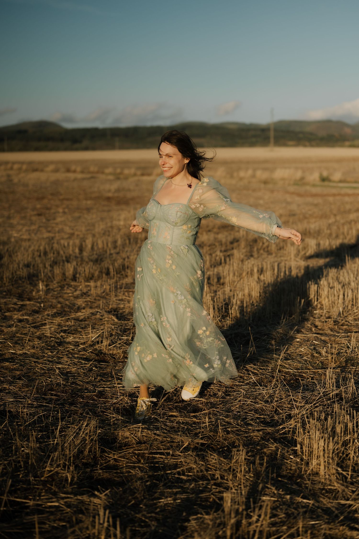 A figure in a flowing blue dress runs through a golden harvested wheat field at sunset.